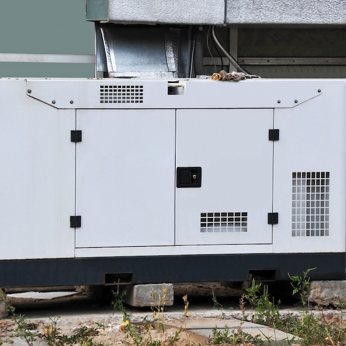 A white electric backup generator is pictured with sparse grass in the foreground