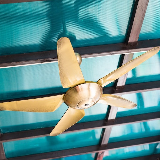 A brand-new ceiling installation. New gold alloy ceiling fan with a robin's egg blue ceiling and dark brown ceiling beams.