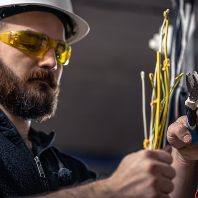 An electrician working on wires wearing yellow goggles and a hard hat.