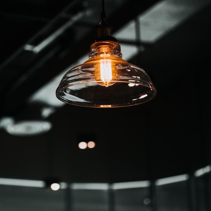 A light fixture with an Edison bulb and a glass shield around the bulb in a dark, moody modern room.